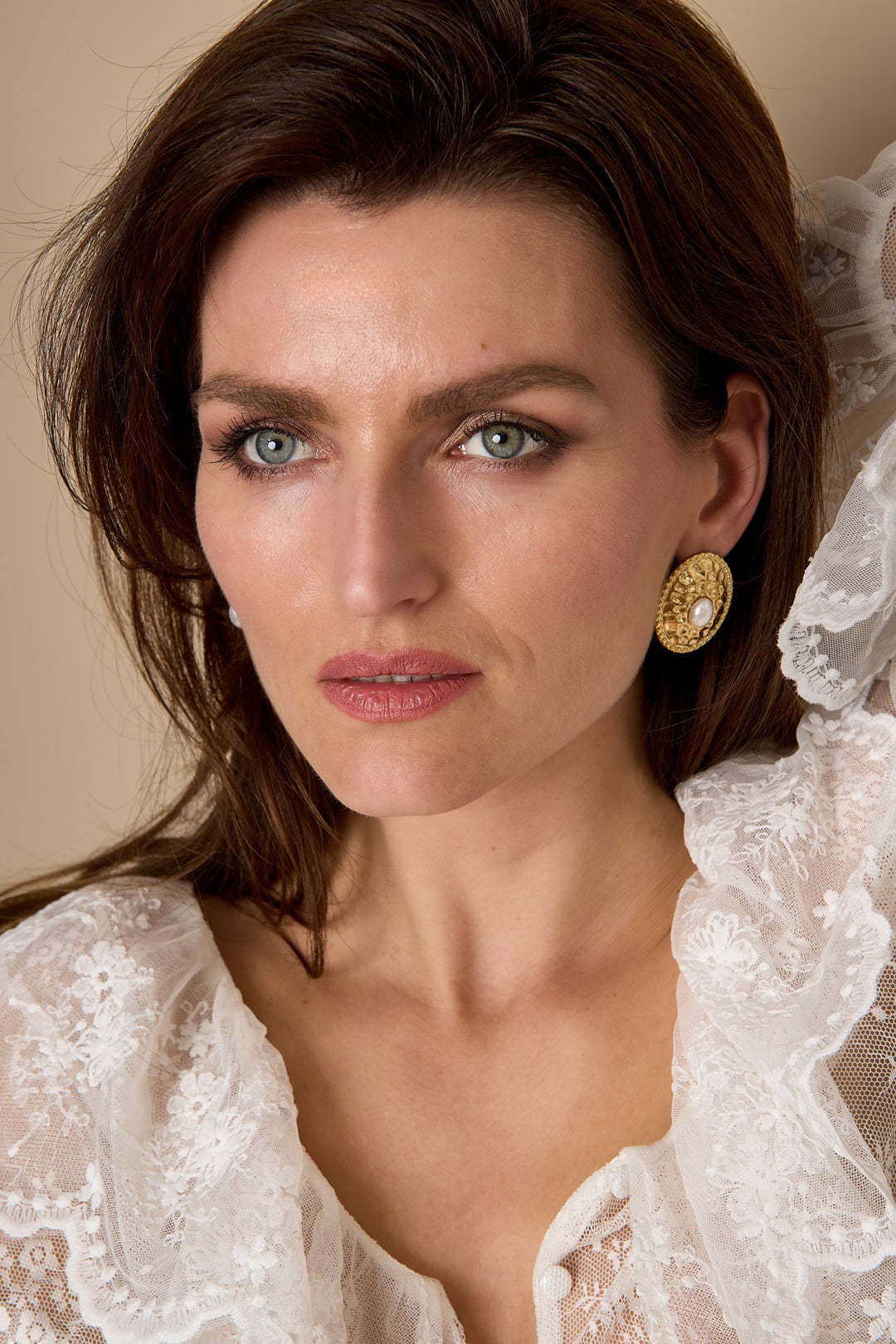 Model wearing gold-tone oval stud earrings with hammered texture and pearl center paired with lace blouse