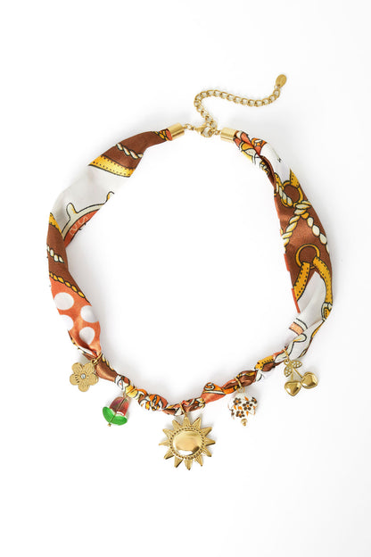 Patterned fabric charm necklace with gold sun, flower, cherry, and bead charms laid flat