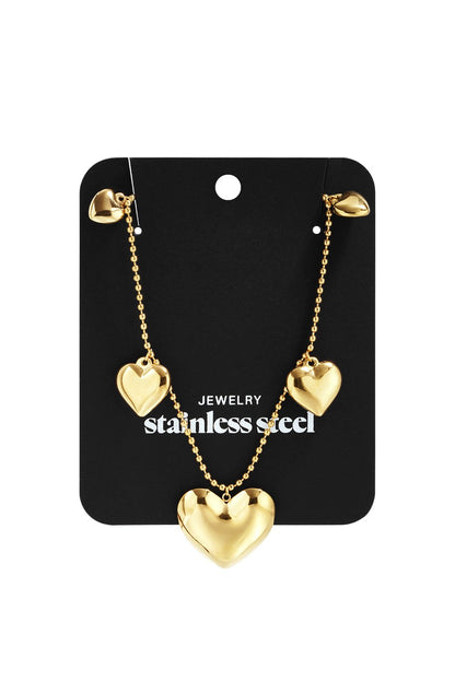 Gold-tone stainless steel chain necklace featuring three polished heart charms on a black display card.