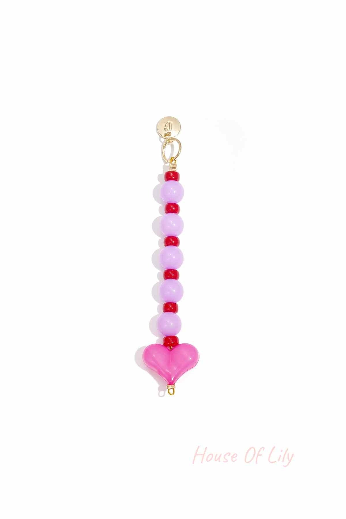 Close-up of pink and red heart bead bag charm with gold clasp on white background