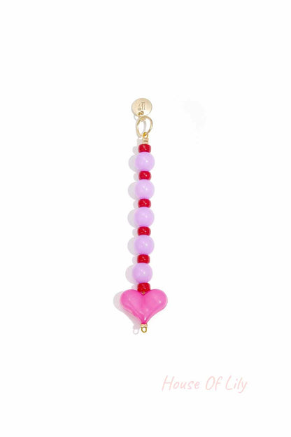 Close-up of pink and red heart bead bag charm with gold clasp on white background