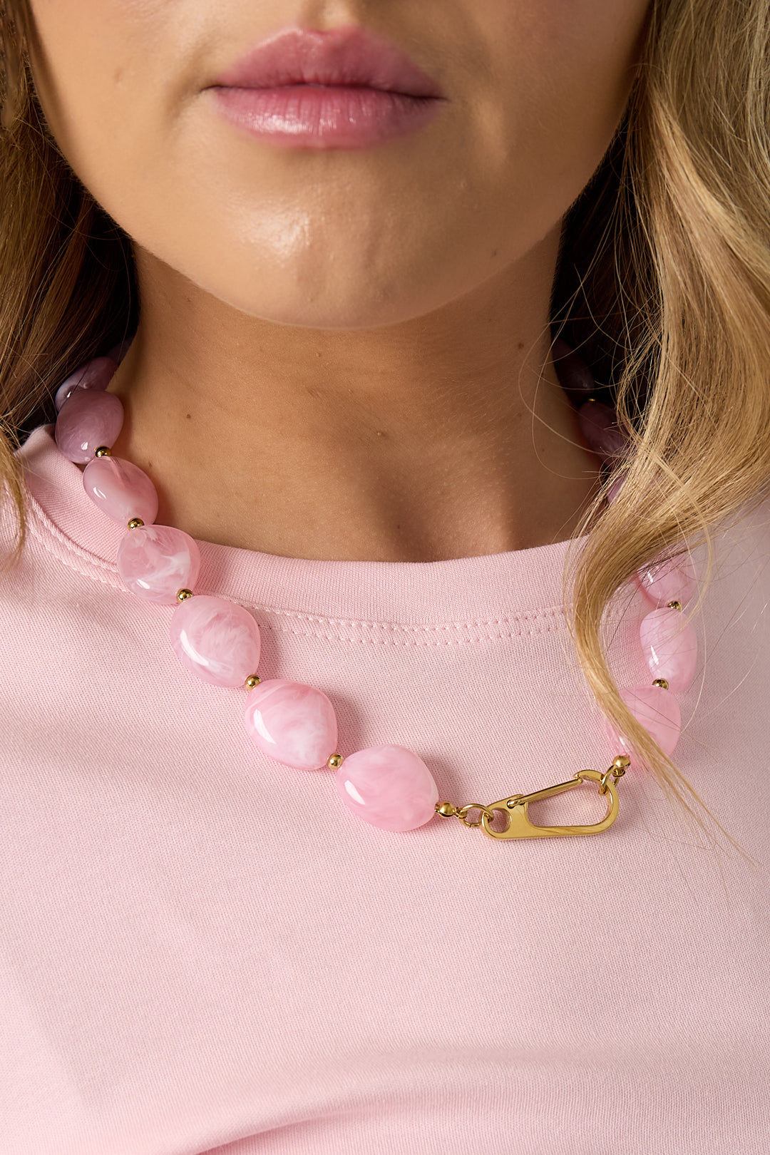 Close-up of pastel pink resin beads and gold-tone spacers in chunky necklace with front clasp on model