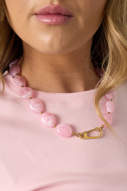 Close-up of pastel pink resin beads and gold-tone spacers in chunky necklace with front clasp on model