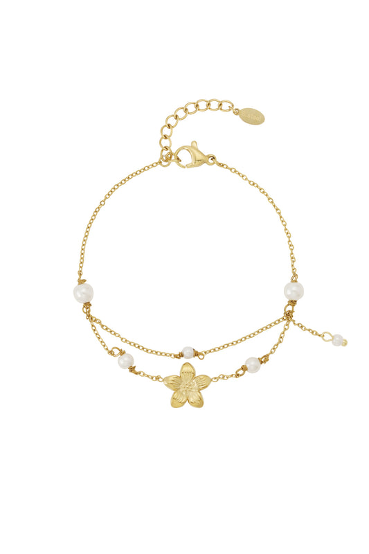 Gold double layer charm bracelet with flower pendant and faux pearls on a white background