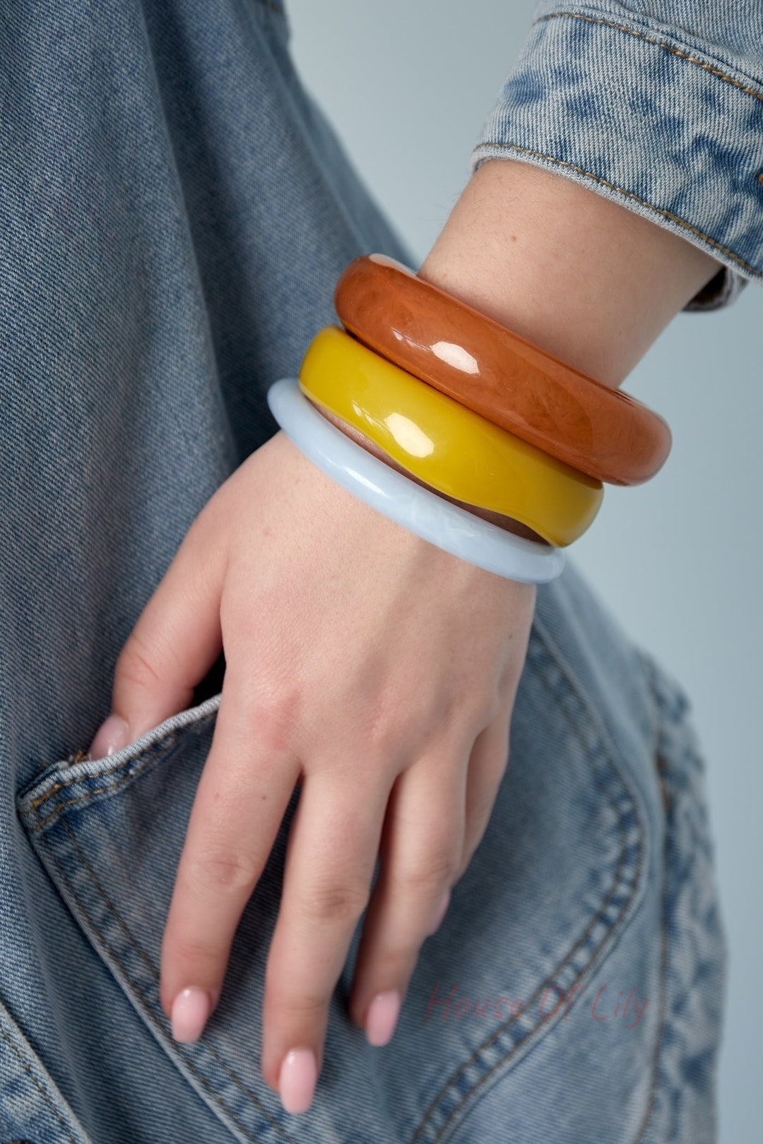 Close-up of a hand wearing three chunky resin bangles in brown, yellow, and light blue with denim jacket