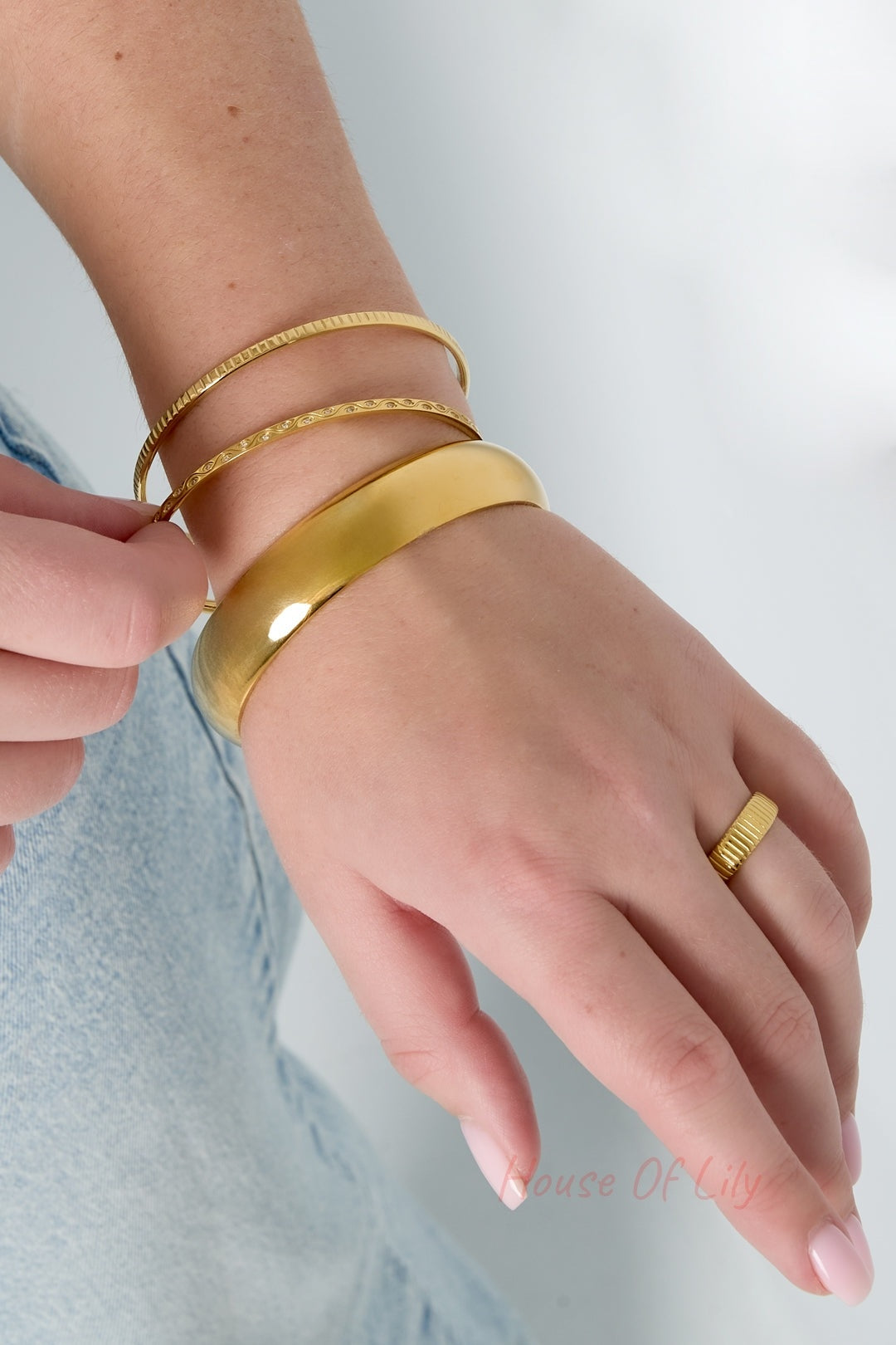 Close-up wrist shot of three gold bangles and a matching gold ring worn together showing coordinated minimalist jewelry style