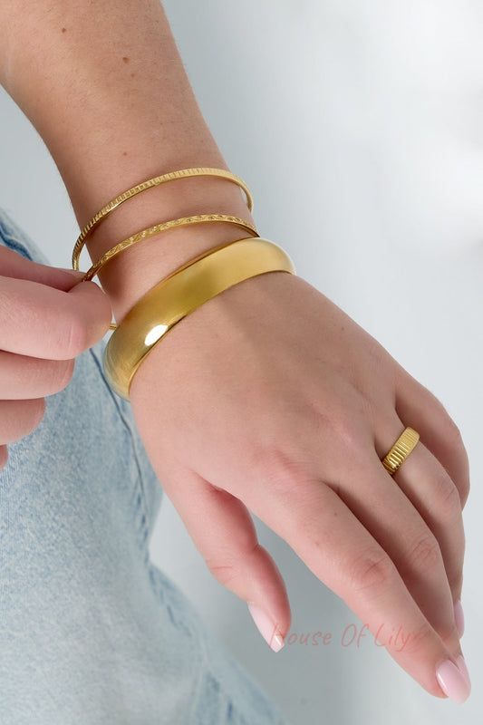 Close-up wrist shot of three gold bangles and a matching gold ring worn together showing coordinated minimalist jewelry style