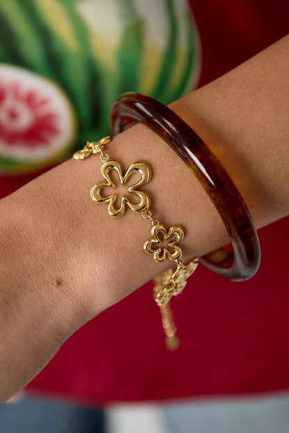 Close-up of gold floral charm bracelet worn on wrist paired with translucent dark brown bangle