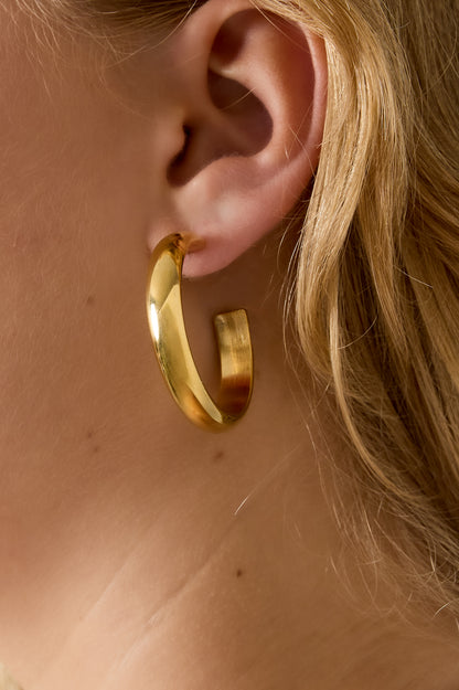 Close-up of a gold chunky hoop earring worn by a woman showcasing its soft and bold style