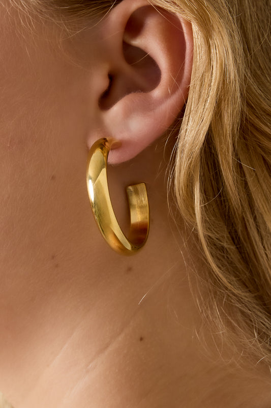 Close-up of a gold chunky hoop earring worn by a woman showcasing its soft and bold style