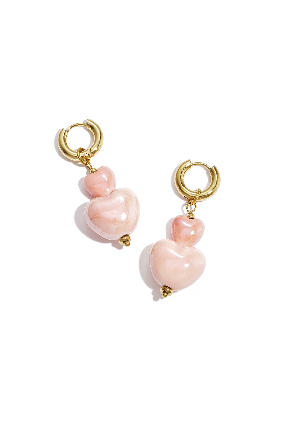Gold hoop earrings with two glossy pink heart-shaped charms dangling against white background