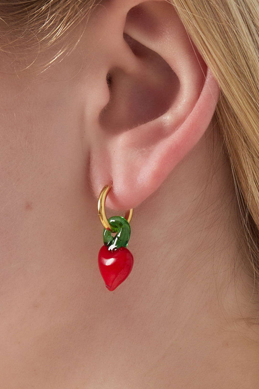 Close-up of a woman's ear wearing gold hoop earring with a red glass berry charm and green stem