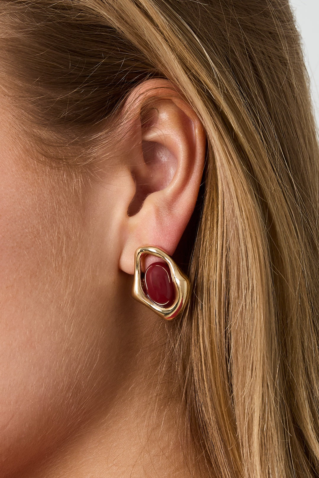 Golden Glitch Hoops: Irregular gold-tone metal earrings featuring a central, polished deep red oval stone.