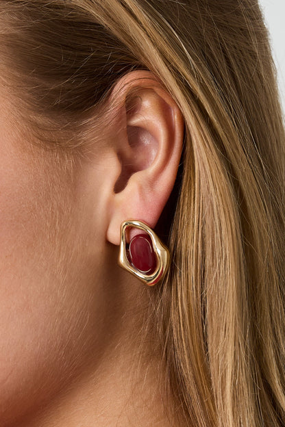 Golden Glitch Hoops: Irregular gold-tone metal earrings featuring a central, polished deep red oval stone.