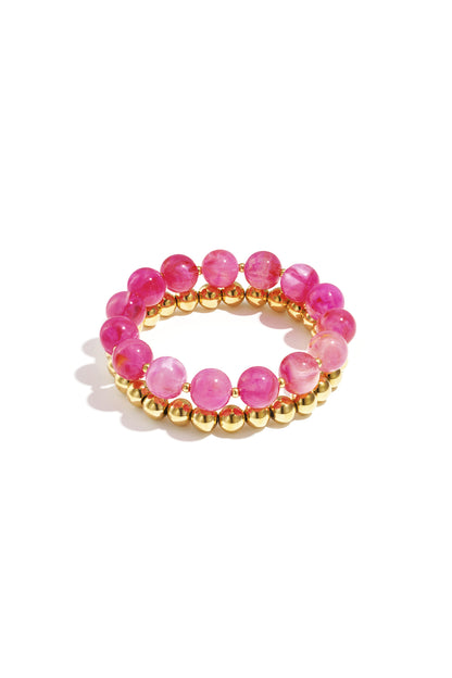 Stack of two bracelets with hot pink round acrylic beads and gold-tone metal beads on white background