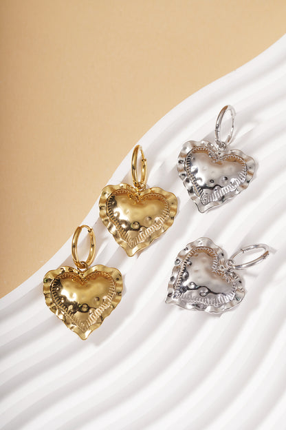 Heart Loop Drops: Gold and silver hoop earrings with textured, ruffled-edge heart charms on a white wavy display.