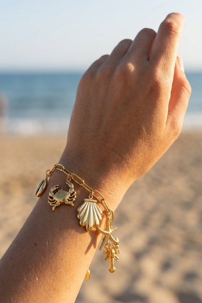 Gold bracelet with charms on a hand by the beach