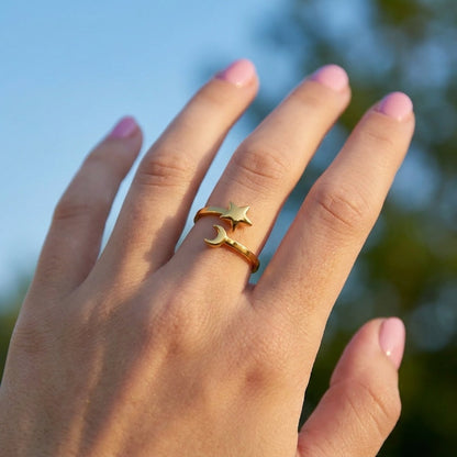 Gold open-style ring featuring a polished star and crescent moon charm worn on a finger.
