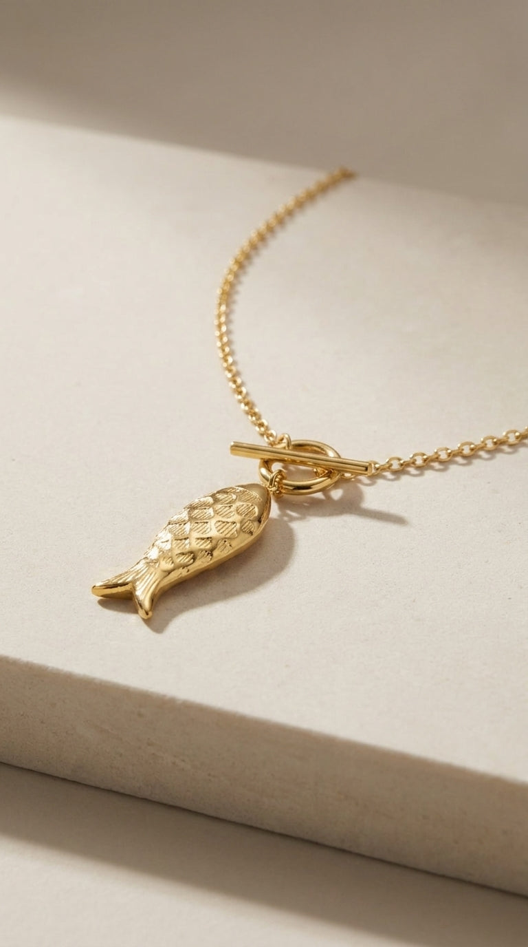Gold tone Catching Vibes necklace featuring a textured fish pendant on a delicate chain with a toggle clasp.