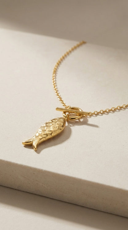 Gold tone Catching Vibes necklace featuring a textured fish pendant on a delicate chain with a toggle clasp.
