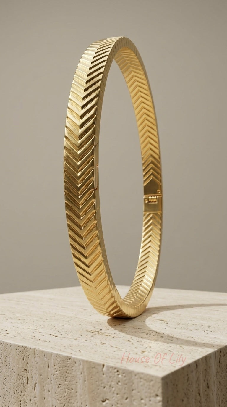Gold-tone hinged bangle featuring a textured chevron pattern, standing upright on a beige stone block.