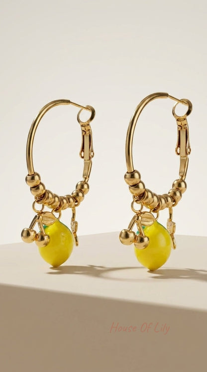 Gold-tone hoop earrings featuring a beaded bottom half with hanging yellow lemon charms and small gold fruit charms.