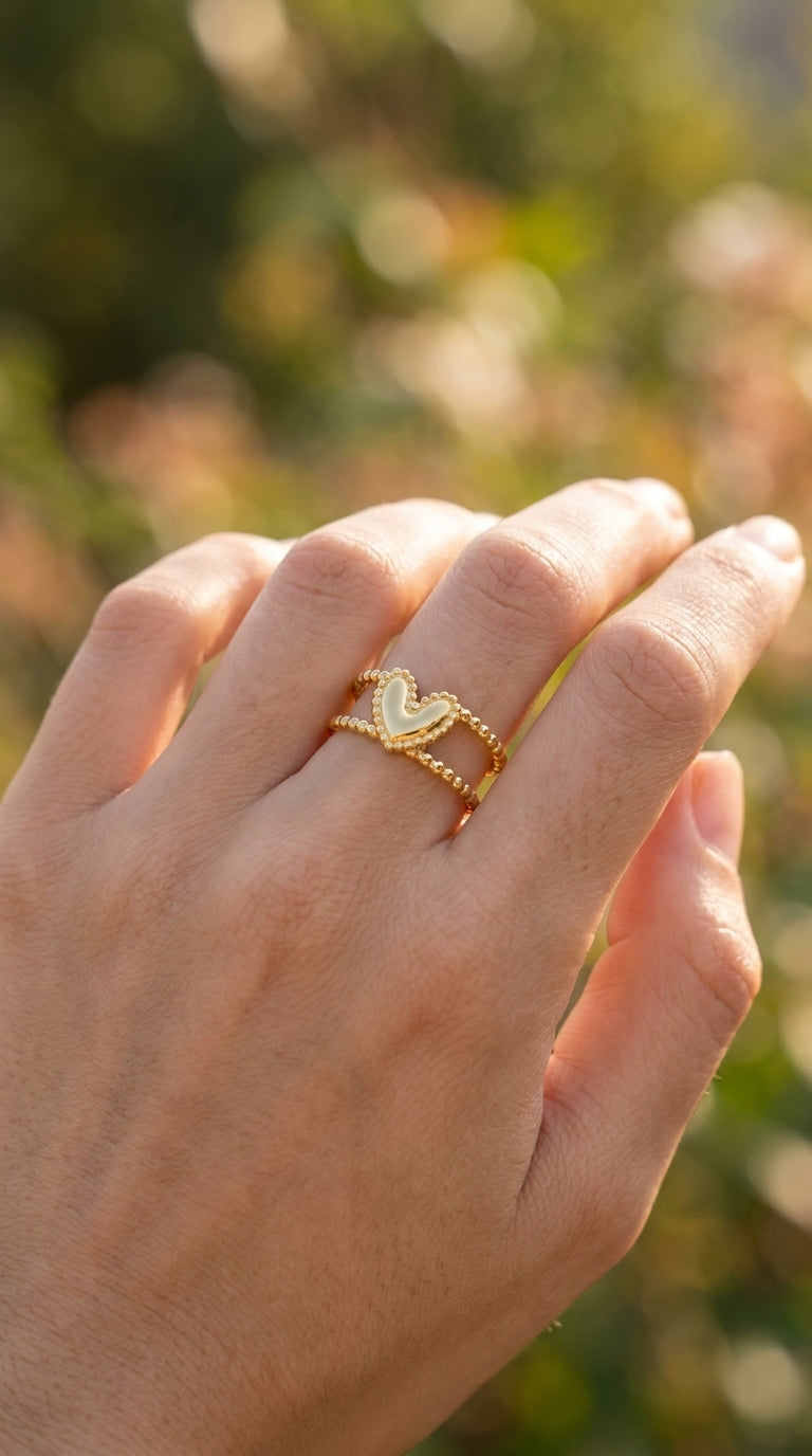 Gold Double Trouble statement ring featuring a heart charm on a dual-beaded band worn on a finger.