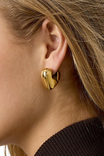 Close-up side view of model's ear featuring chunky gold heart hoop earring in bright lighting