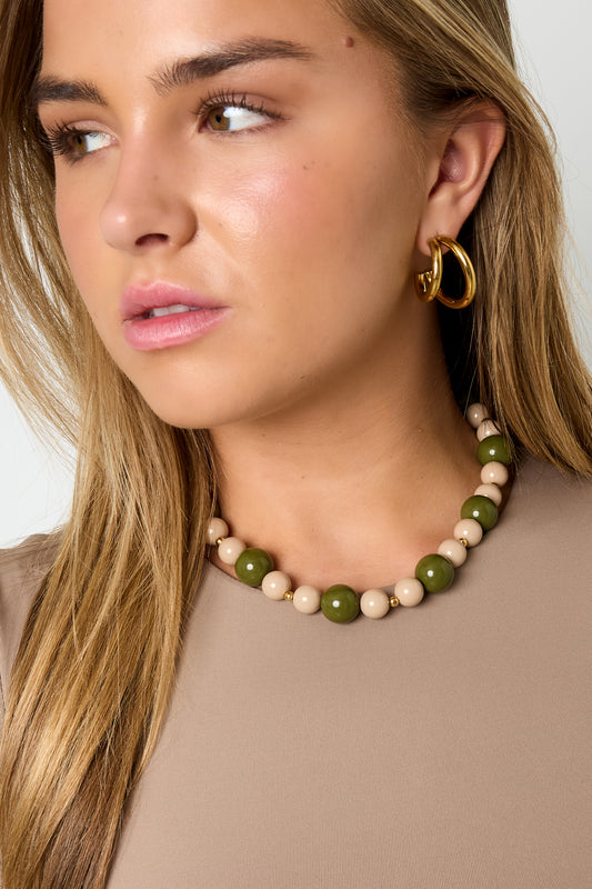 Model wearing green and cream chunky beaded necklace and gold hoop earrings with beige top