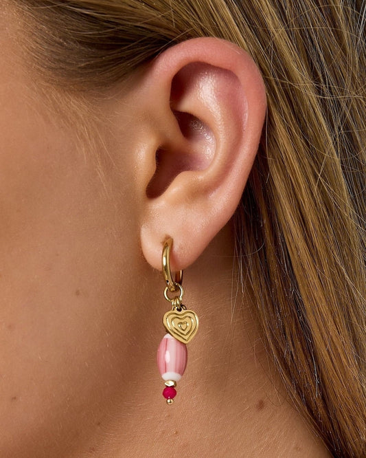 Close-up ear shot showing gold hoop earring with pink beaded charm and gold heart detail on a woman with light skin and blonde hair