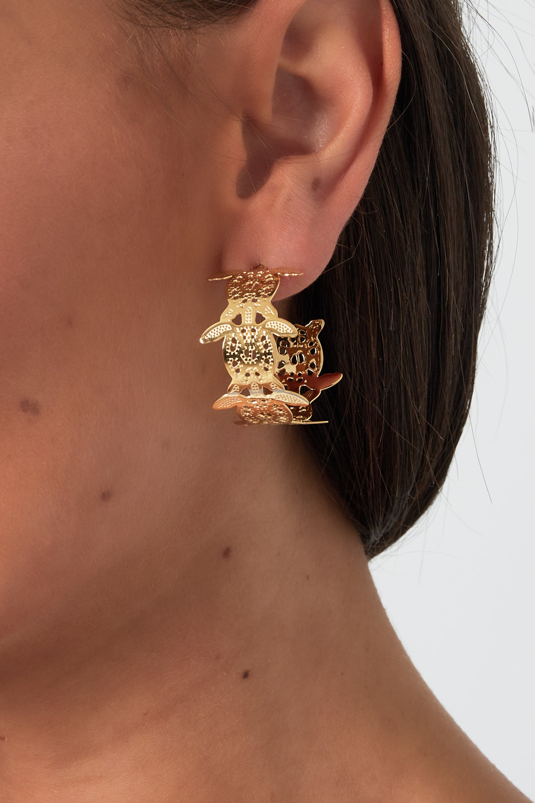 Close-up view of a woman wearing gold-plated turtle motif hoop earring on her ear