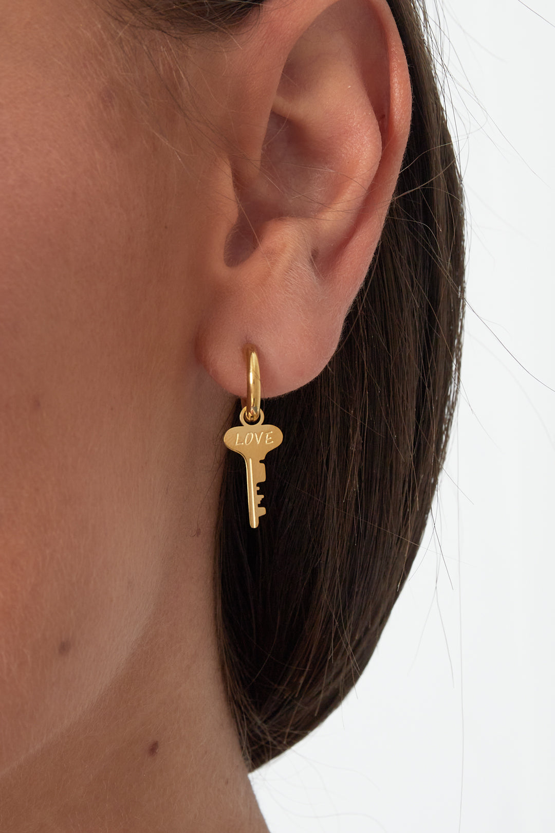 Close-up of a woman wearing gold hoop earring with a key charm engraved 'LOVE', showcasing the earring's size and fit