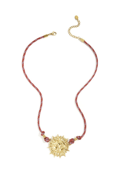 Gold-tone sun pendant necklace with red rope cord featuring blue and white accents laid flat