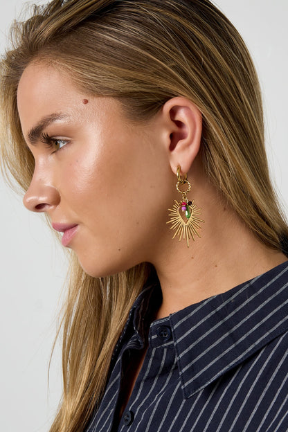 Side profile of woman wearing gold-tone radiant heart charm drop earring showing sunburst and colorful beads