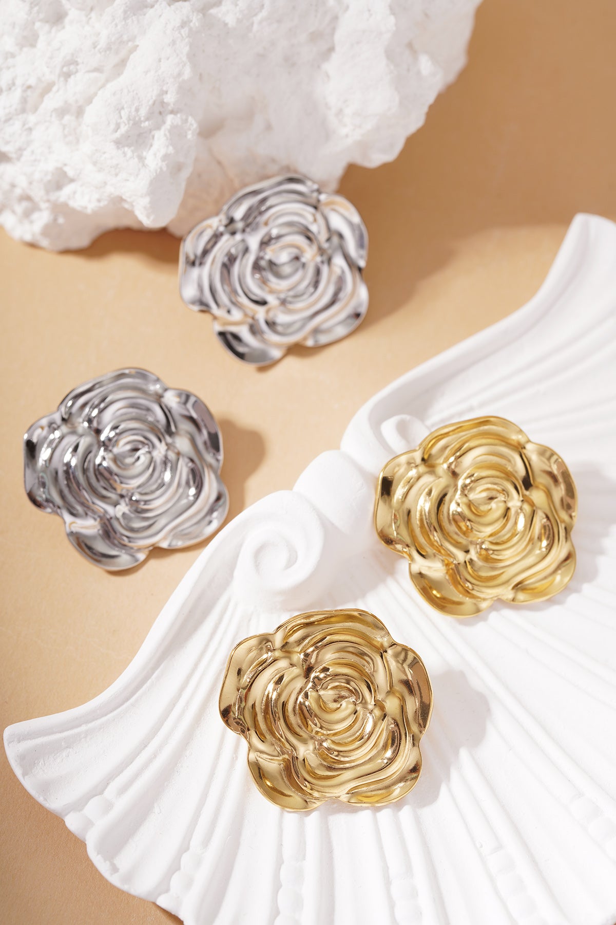 Bloom Core Studs: Two pairs of metallic rose-shaped earrings in polished gold and silver finishes on a shell dish.