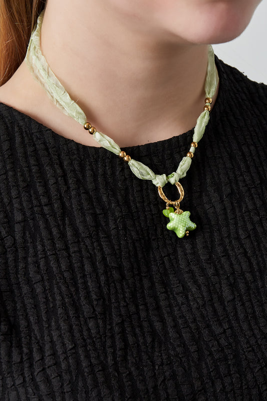 Woman wearing playful sea star necklace with green fabric and gold beads paired with black textured top