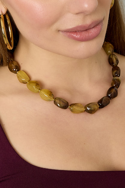 Detail of amber and chocolate acrylic beaded necklace with glossy finish on woman in maroon top