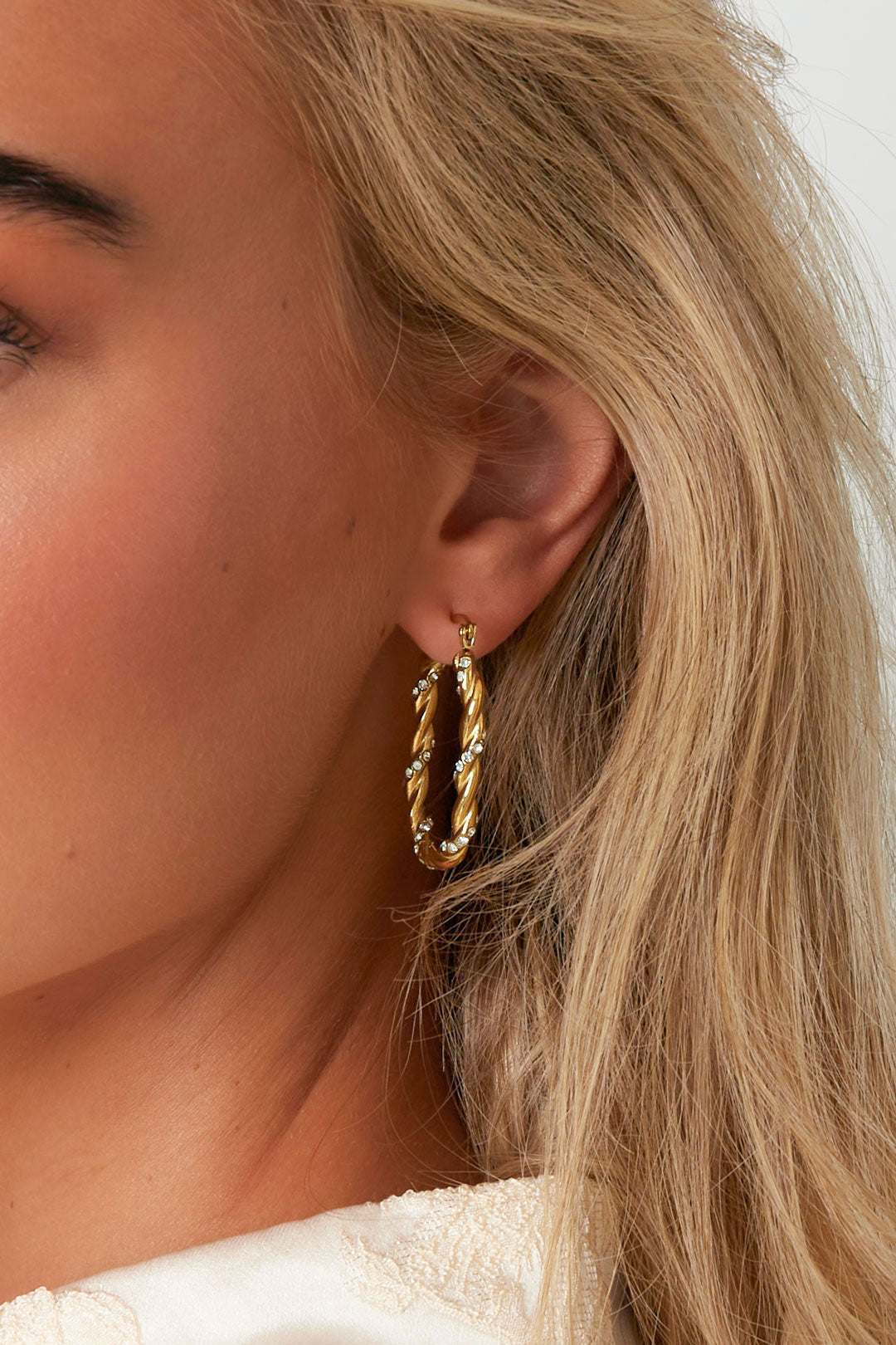 Woman wearing the gold twisted rhinestone hoop earrings showcasing their size and sparkle