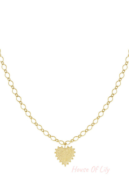 Close-up of a gold-tone heart pendant necklace with textured surface and bead accents on a twisted chain, isolated on white background