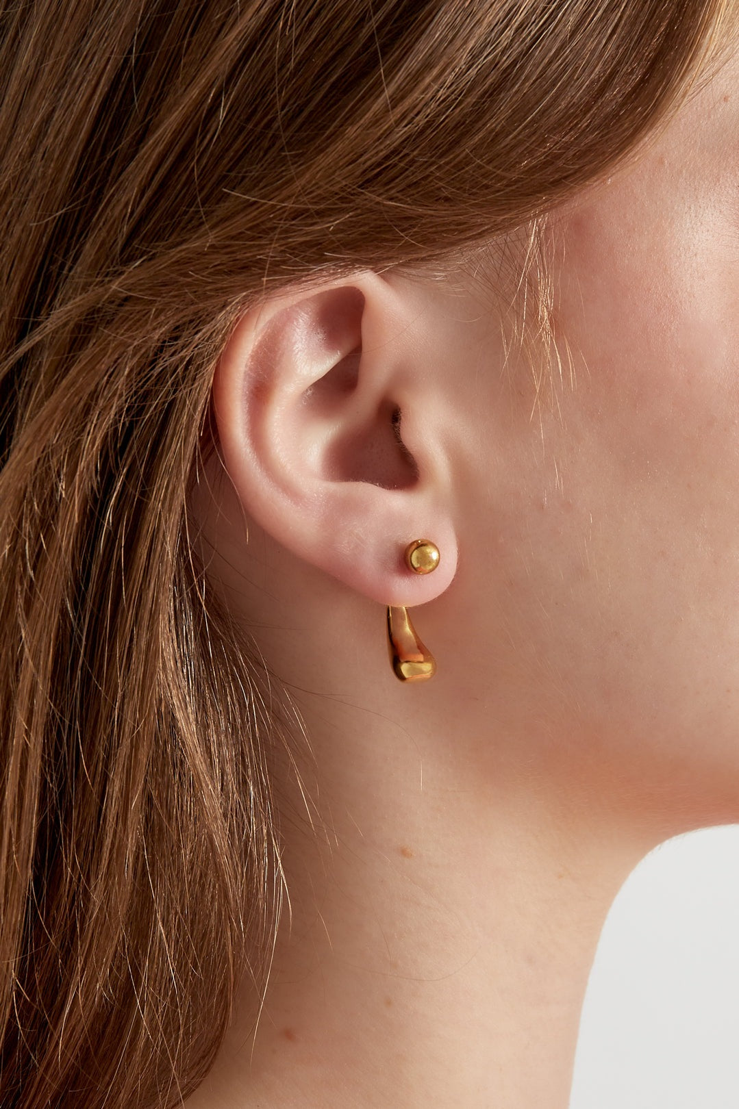 Close-up of a woman wearing a gold teardrop stud earring showing the delicate drop detail