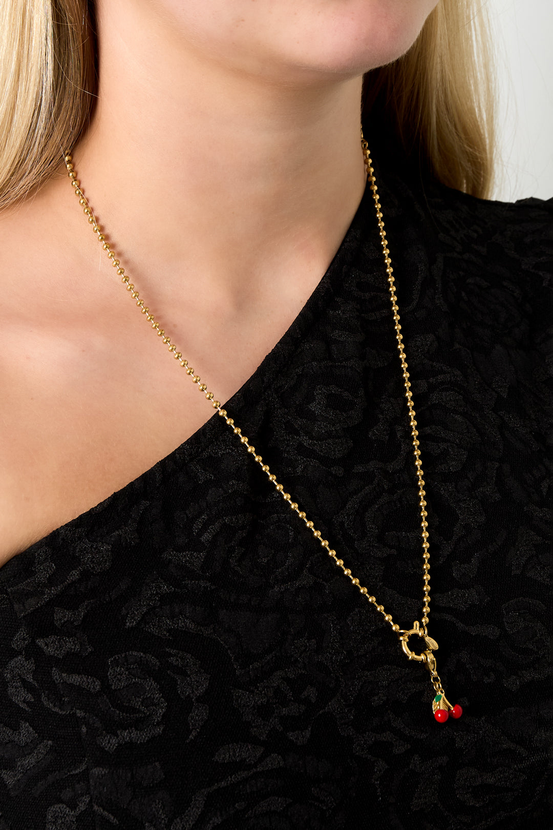 Model wearing gold bead chain necklace with cherry charm pendant over black top