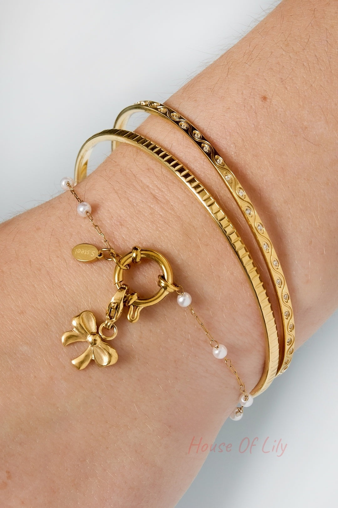 Wrist wearing layered gold bangles with a pearl charm bracelet including a bow charm