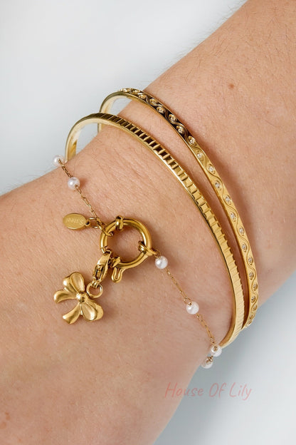 Wrist wearing layered gold bangles with a pearl charm bracelet including a bow charm