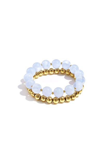 Stack of two bracelets with pale blue round acrylic beads and gold-tone metal beads on white background