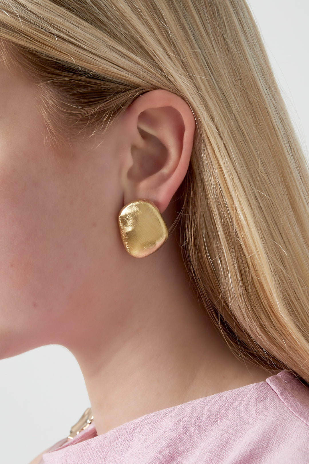 Side view of a woman wearing a single brushed gold organic pebble stud earring paired with light pink blouse