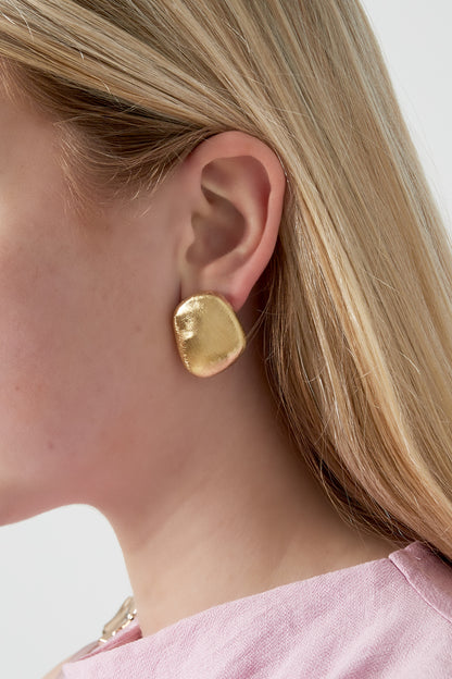 Side view of a woman wearing a single brushed gold organic pebble stud earring paired with light pink blouse