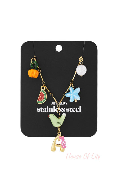 Gold stainless steel charm necklace featuring a letter "A" pendant, bird, watermelon slice, flower, and assorted beads.