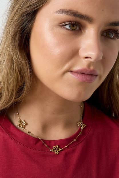 Model wearing the gold flower charm necklace paired with a red top, showcasing the necklace around her neck