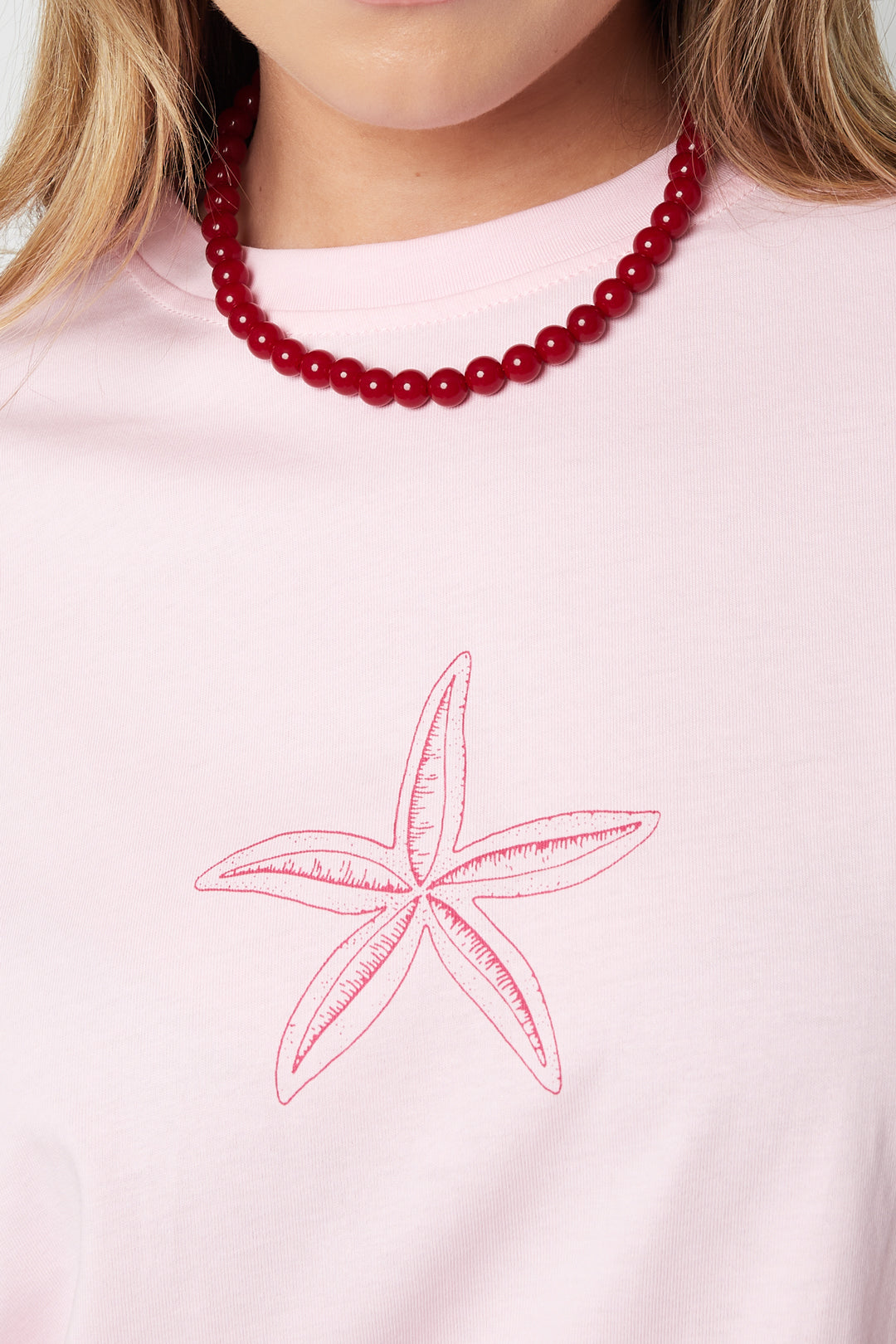Close-up of red resin beads necklace worn by a woman in a pink starfish print shirt