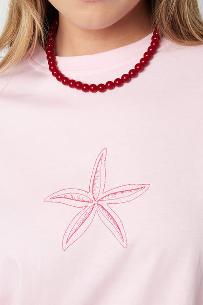 Close-up of red resin beads necklace worn by a woman in a pink starfish print shirt